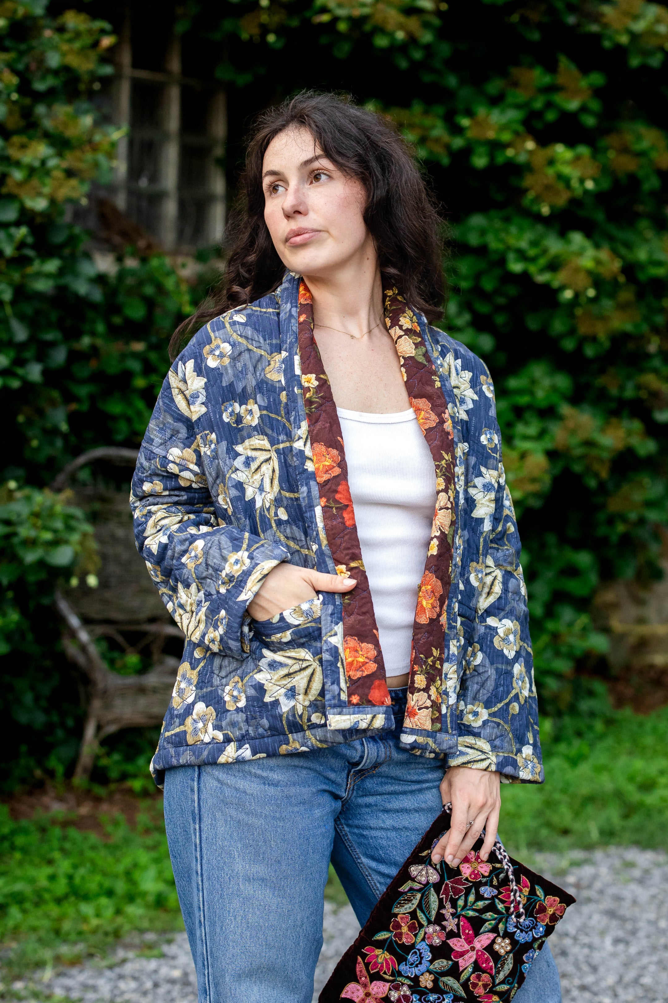 Woman wearing a floral kimono-style jacket outdoors with greenery in the background