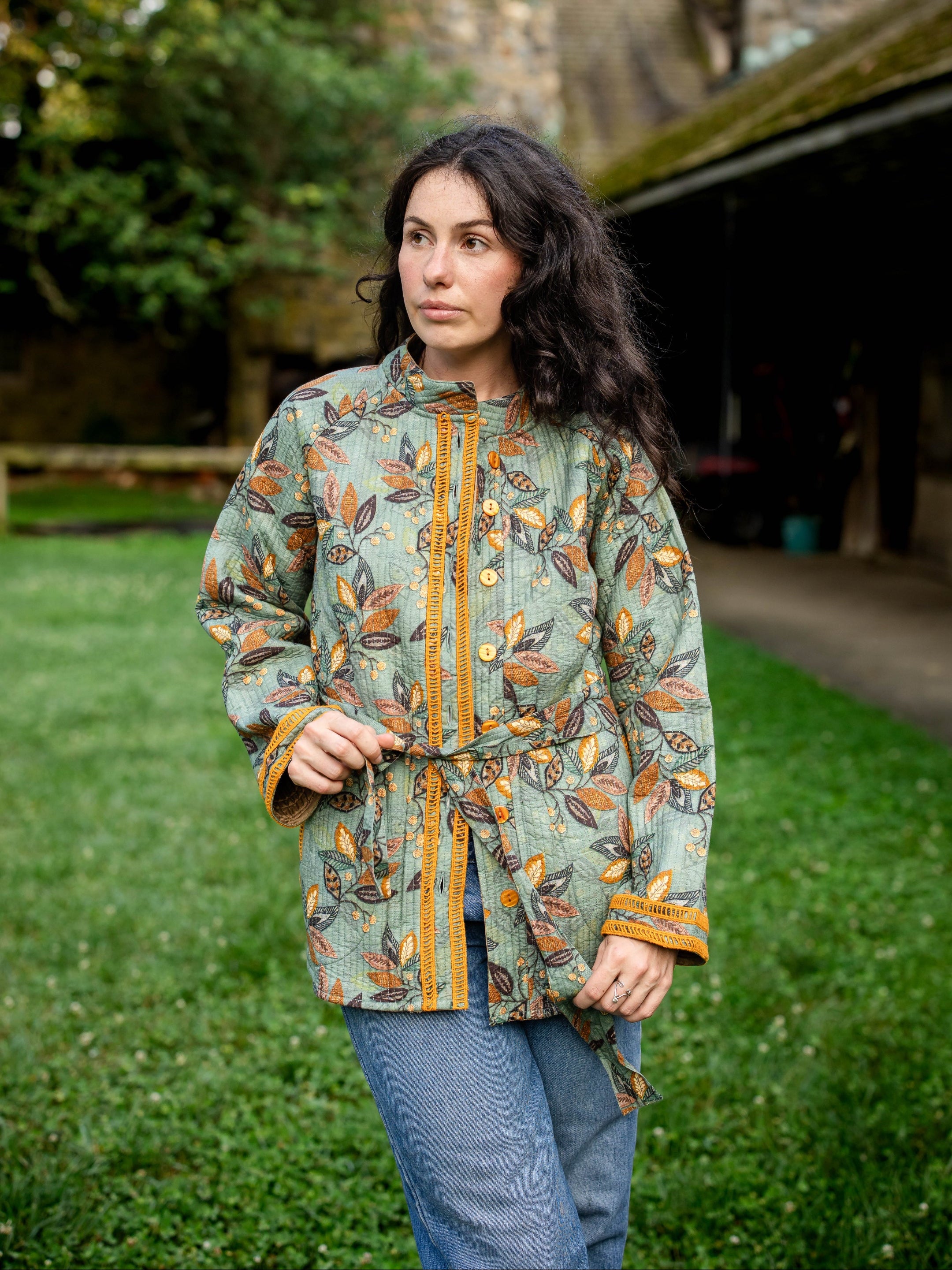 Woman wearing a patterned jacket outdoors with green grass and a building in the background